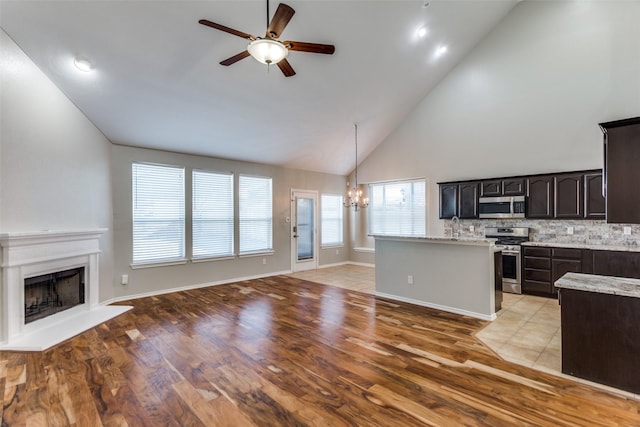 kitchen with ceiling fan with notable chandelier, backsplash, stainless steel appliances, high vaulted ceiling, and decorative light fixtures