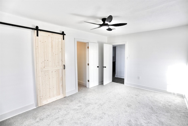 unfurnished bedroom featuring ceiling fan, a barn door, and light carpet