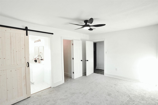 unfurnished bedroom with ensuite bathroom, a barn door, light colored carpet, and ceiling fan