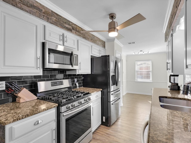 kitchen with sink, appliances with stainless steel finishes, dark stone countertops, ornamental molding, and white cabinets