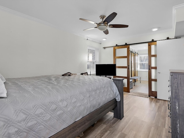 bedroom with multiple windows, a barn door, light wood-type flooring, and ceiling fan