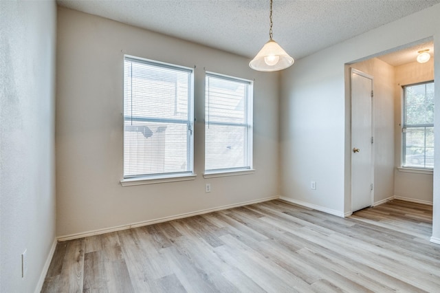 spare room with a textured ceiling, light wood-type flooring, and baseboards