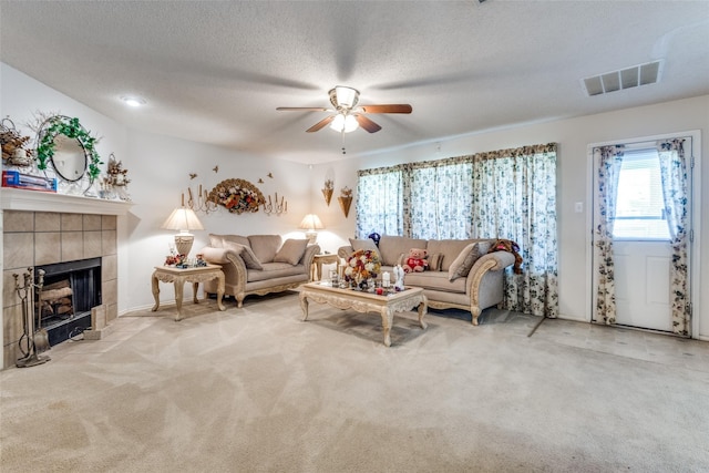 carpeted living room with ceiling fan, a tiled fireplace, and a textured ceiling