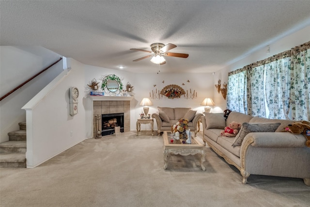 living room featuring a textured ceiling, carpet floors, a tile fireplace, and ceiling fan