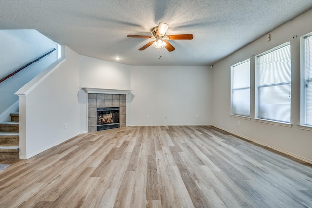 unfurnished living room featuring light wood-style floors, ceiling fan, a fireplace, and stairway