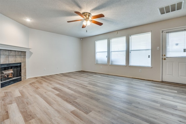 unfurnished living room featuring plenty of natural light, a tiled fireplace, wood finished floors, and visible vents