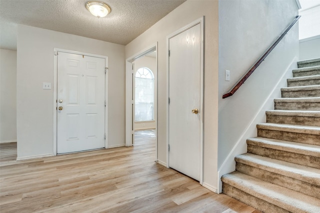 foyer entrance with a textured ceiling, stairway, baseboards, and light wood-style floors