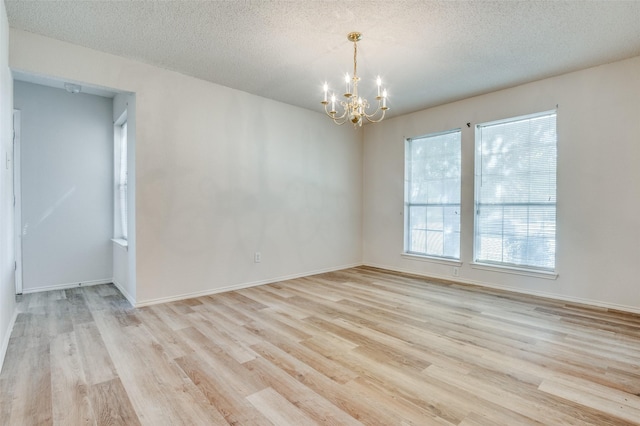 empty room featuring light wood-style floors, baseboards, a chandelier, and a textured ceiling