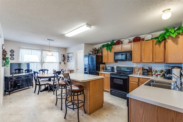 kitchen with sink, a breakfast bar, hanging light fixtures, a center island, and black appliances