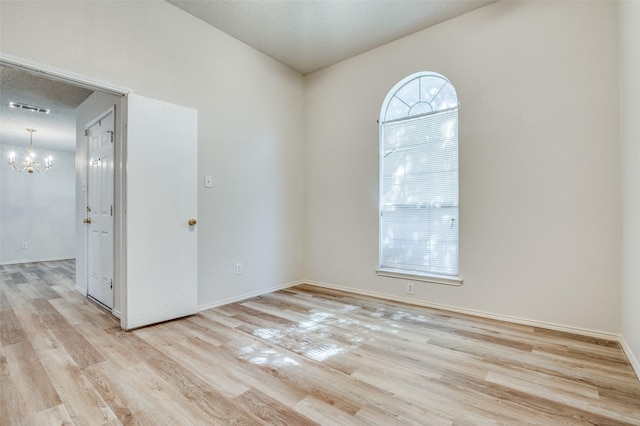 spare room with a textured ceiling, visible vents, baseboards, light wood-style floors, and an inviting chandelier