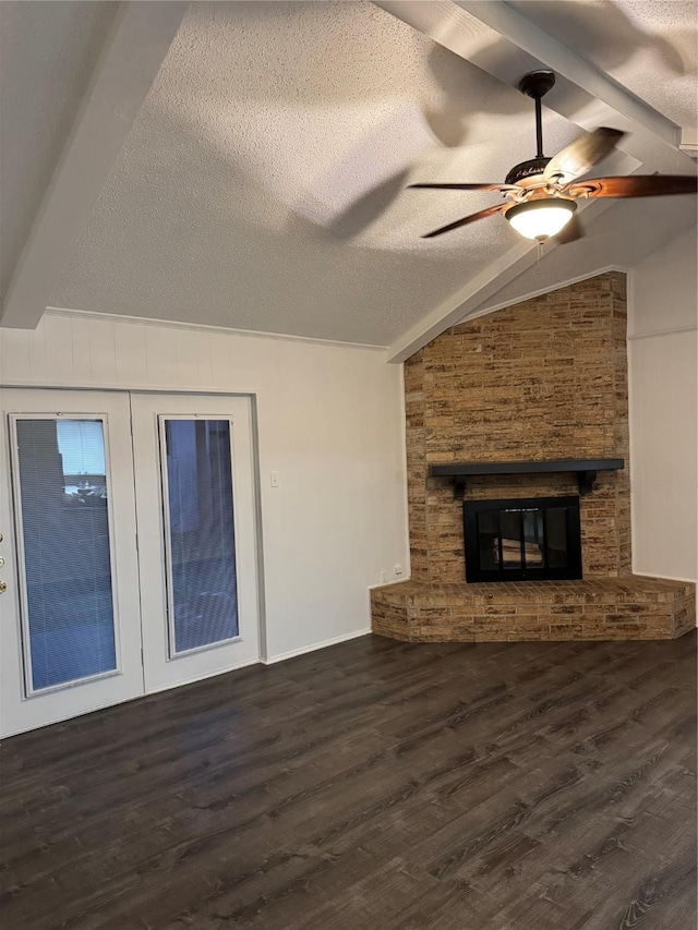 unfurnished living room with a stone fireplace, vaulted ceiling with beams, ceiling fan, dark wood-type flooring, and a textured ceiling