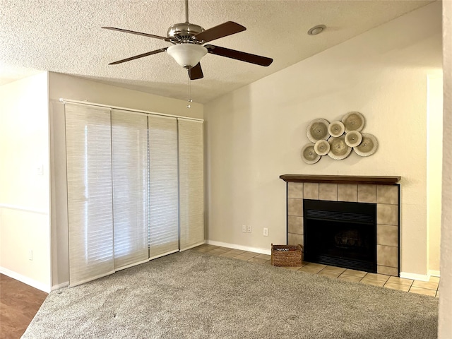 unfurnished living room with ceiling fan, carpet flooring, a tiled fireplace, and a textured ceiling