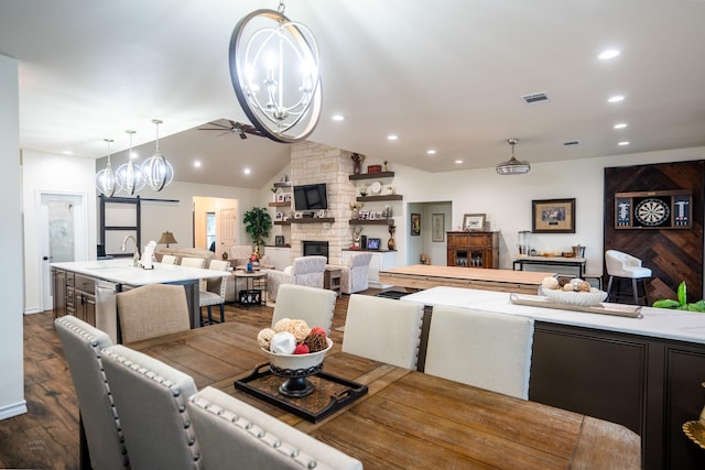 dining room with vaulted ceiling, dark hardwood / wood-style floors, ceiling fan with notable chandelier, a fireplace, and sink