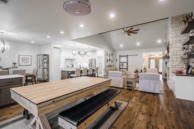 dining space featuring dark hardwood / wood-style floors, lofted ceiling, a barn door, and ceiling fan with notable chandelier