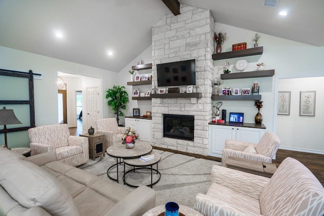 living room featuring wood-type flooring, a barn door, vaulted ceiling with beams, and a stone fireplace