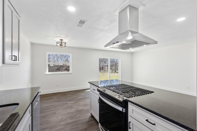 kitchen featuring white cabinetry, appliances with stainless steel finishes, island range hood, and dark stone countertops