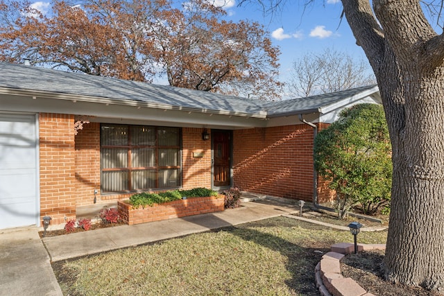 view of exterior entry featuring a garage and a lawn