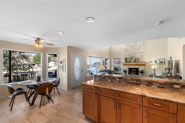 kitchen with ceiling fan, a stone fireplace, light tile patterned floors, and light stone counters