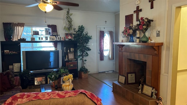 living room featuring a tiled fireplace, crown molding, wood-type flooring, and ceiling fan