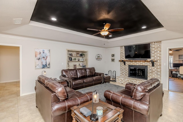 tiled living room with built in shelves, ceiling fan, and a tray ceiling