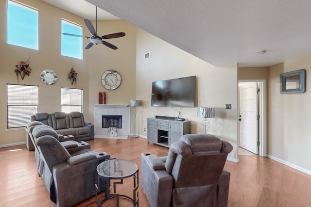 living room with a high ceiling, a fireplace, ceiling fan, and light wood-type flooring