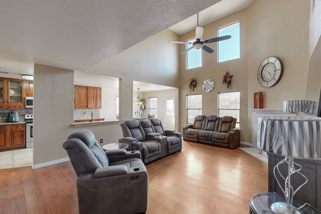 living room with a high ceiling, ceiling fan, and light hardwood / wood-style flooring