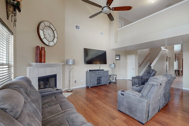 living room with crown molding, a tile fireplace, ceiling fan, a high ceiling, and wood-type flooring