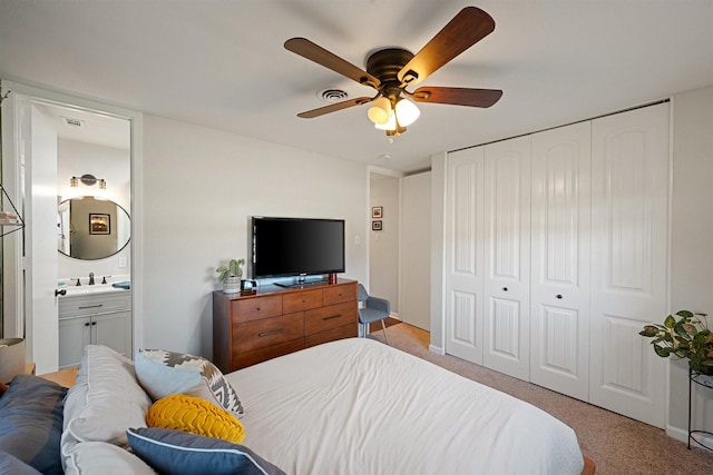 carpeted bedroom with sink, ensuite bath, a closet, and ceiling fan