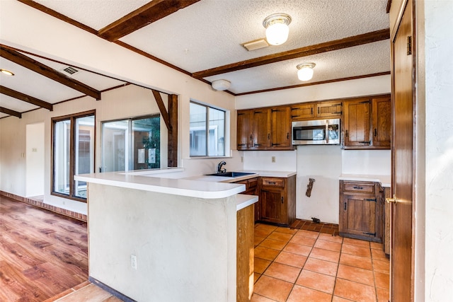 kitchen featuring sink, beam ceiling, a textured ceiling, light tile patterned flooring, and kitchen peninsula