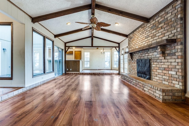 unfurnished living room featuring lofted ceiling with beams, a brick fireplace, a textured ceiling, ceiling fan, and hardwood / wood-style floors