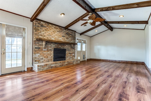 unfurnished living room with lofted ceiling with beams, a brick fireplace, a textured ceiling, ceiling fan, and hardwood / wood-style floors