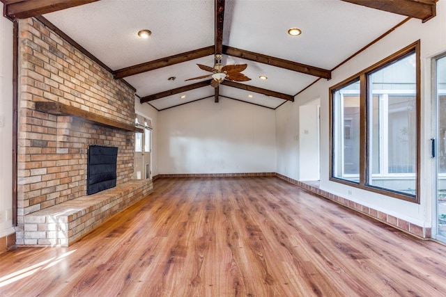 unfurnished living room with lofted ceiling with beams, ceiling fan, light hardwood / wood-style floors, a brick fireplace, and a textured ceiling