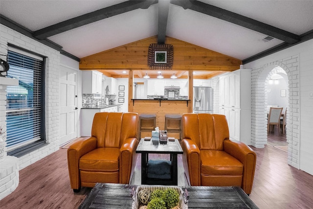 living room with lofted ceiling with beams, brick wall, and dark hardwood / wood-style floors