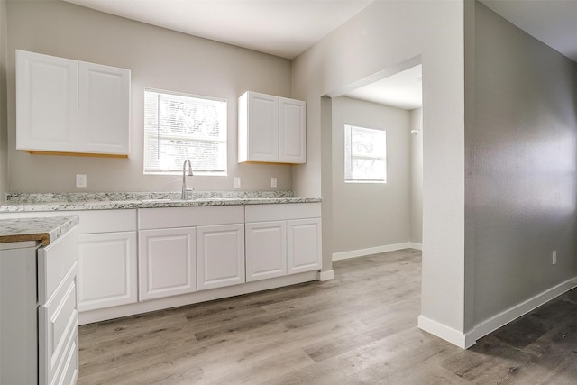 kitchen featuring sink, light hardwood / wood-style floors, white cabinets, and light stone countertops