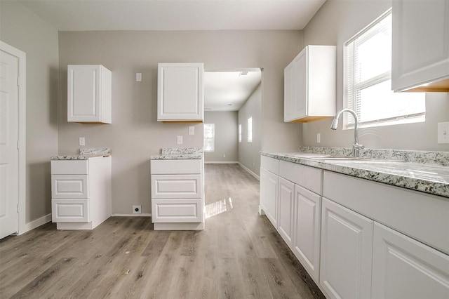 kitchen featuring white cabinetry, light stone counters, sink, and light hardwood / wood-style flooring