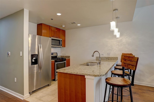 kitchen with appliances with stainless steel finishes, pendant lighting, sink, a kitchen bar, and kitchen peninsula