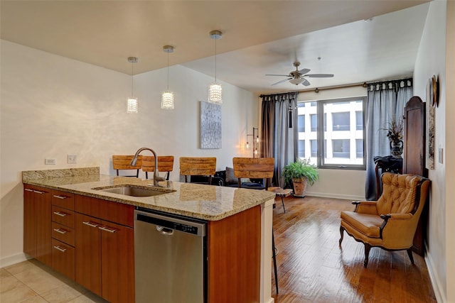 kitchen with pendant lighting, sink, dishwasher, light stone countertops, and kitchen peninsula