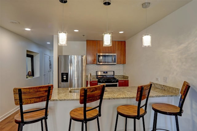 kitchen featuring a breakfast bar area, hanging light fixtures, appliances with stainless steel finishes, kitchen peninsula, and decorative backsplash