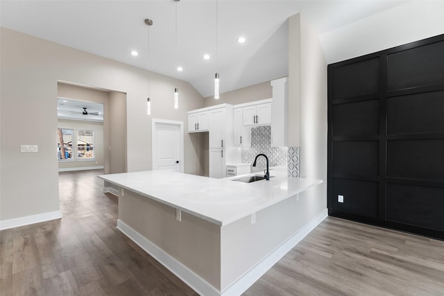 kitchen with pendant lighting, tasteful backsplash, white cabinetry, sink, and light hardwood / wood-style floors