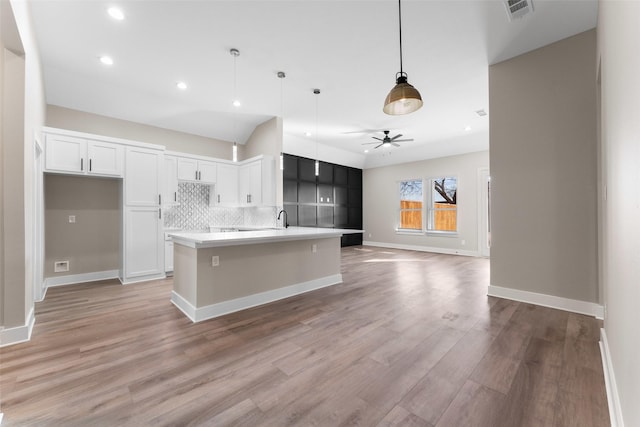 kitchen featuring pendant lighting, white cabinetry, backsplash, a center island with sink, and light wood-type flooring