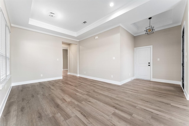 spare room featuring crown molding, a raised ceiling, an inviting chandelier, and light hardwood / wood-style flooring