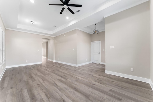 unfurnished room featuring ceiling fan with notable chandelier, ornamental molding, light hardwood / wood-style floors, and a raised ceiling