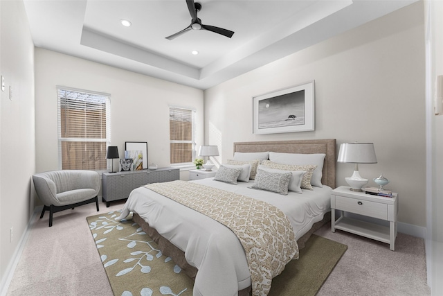 bedroom with a raised ceiling, light carpet, and ceiling fan