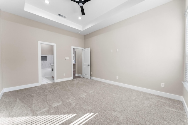 unfurnished bedroom featuring ceiling fan, a tray ceiling, connected bathroom, and light carpet