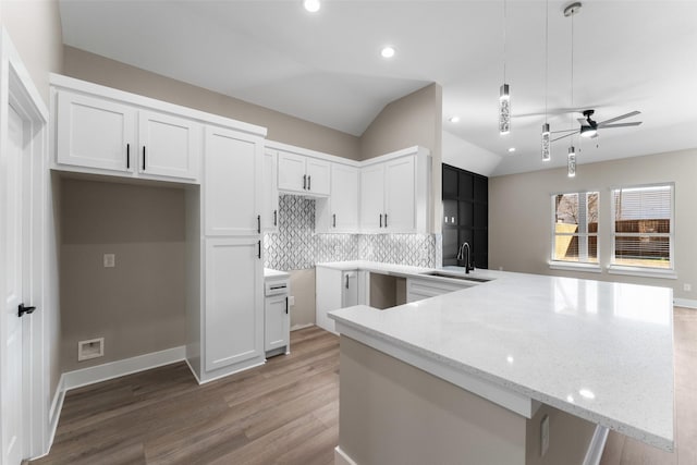 kitchen with vaulted ceiling, pendant lighting, light stone countertops, decorative backsplash, and white cabinets