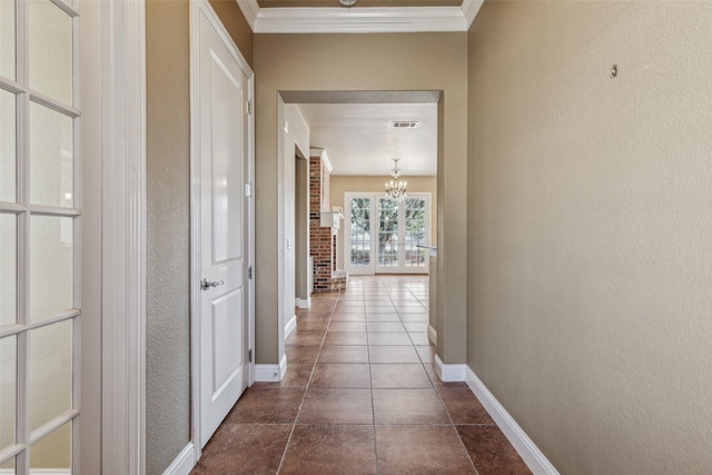 hallway with crown molding, dark tile patterned flooring, and a chandelier