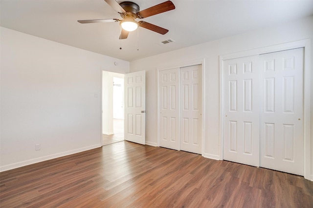 unfurnished bedroom with ceiling fan, dark hardwood / wood-style flooring, and two closets