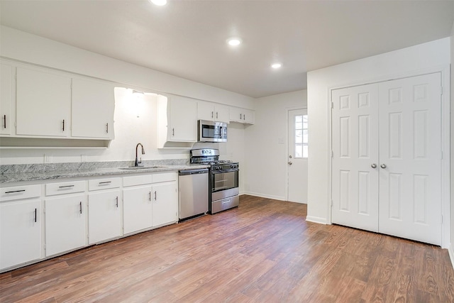 kitchen with appliances with stainless steel finishes, sink, white cabinets, and light hardwood / wood-style floors