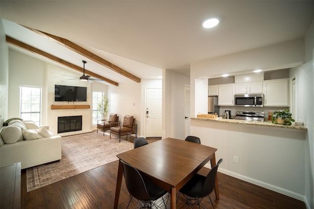 dining area with dark wood-type flooring, ceiling fan, a fireplace, and lofted ceiling with beams