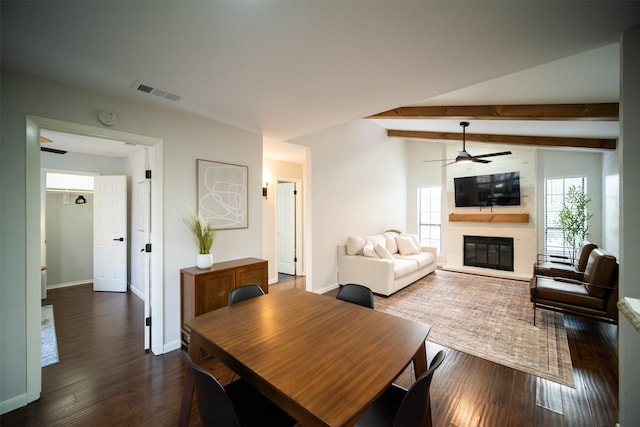 dining space with ceiling fan, a fireplace, dark hardwood / wood-style flooring, and vaulted ceiling with beams